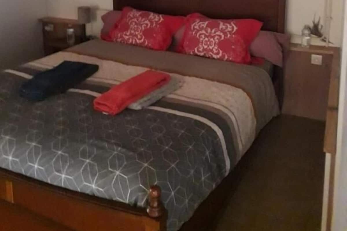 Un dormitorio con cama de madera, una ventana pequeña y una mesita de noche con lámpara.