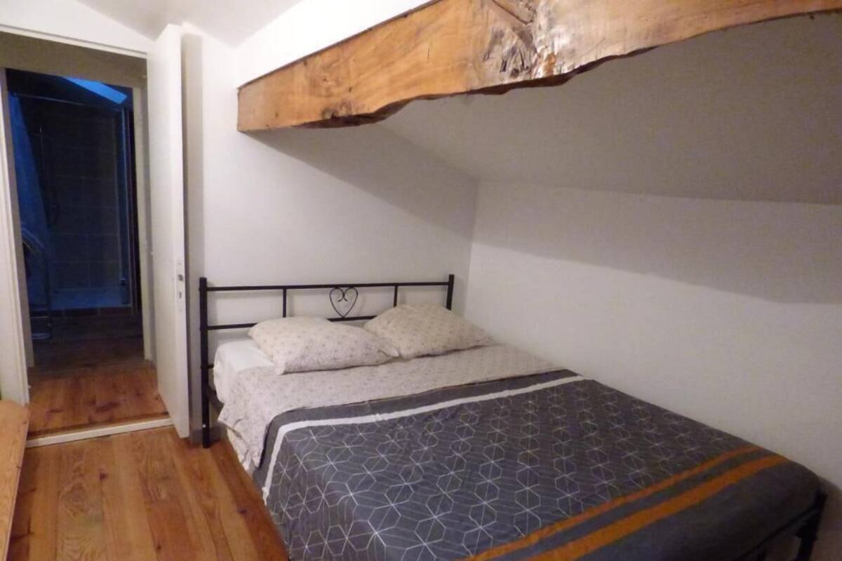 Una cama individual con estructura metálica y un edredón estampado, una viga de techo de madera y suelo de madera.