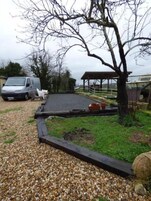 Un camino de grava que conduce a un área de estacionamiento techada, con un vehículo estacionado cerca.