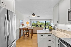 Una cocina moderna con armarios blancos, encimera de mármol y zona de comedor con mesa y sillas.