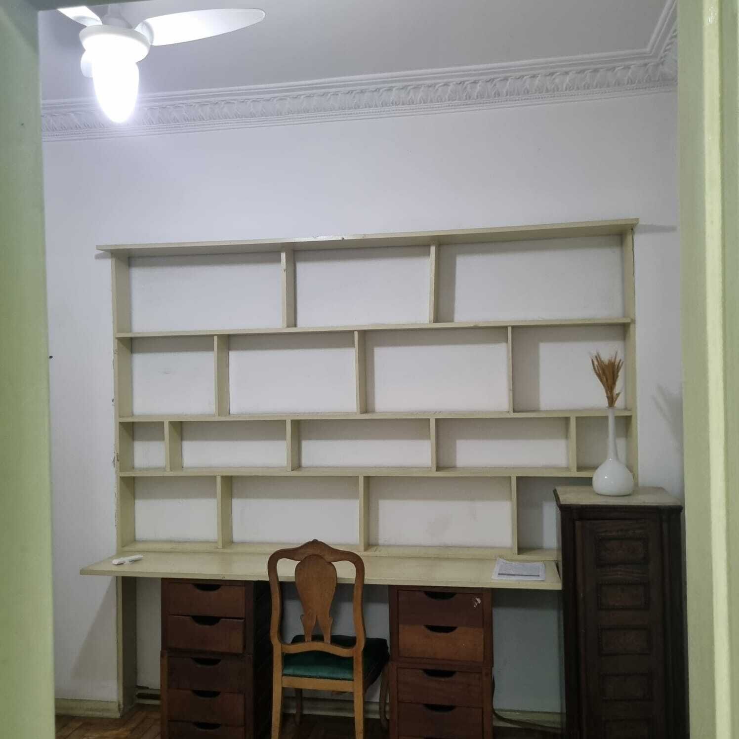 Um quarto com escrivaninha, cadeira e estante.