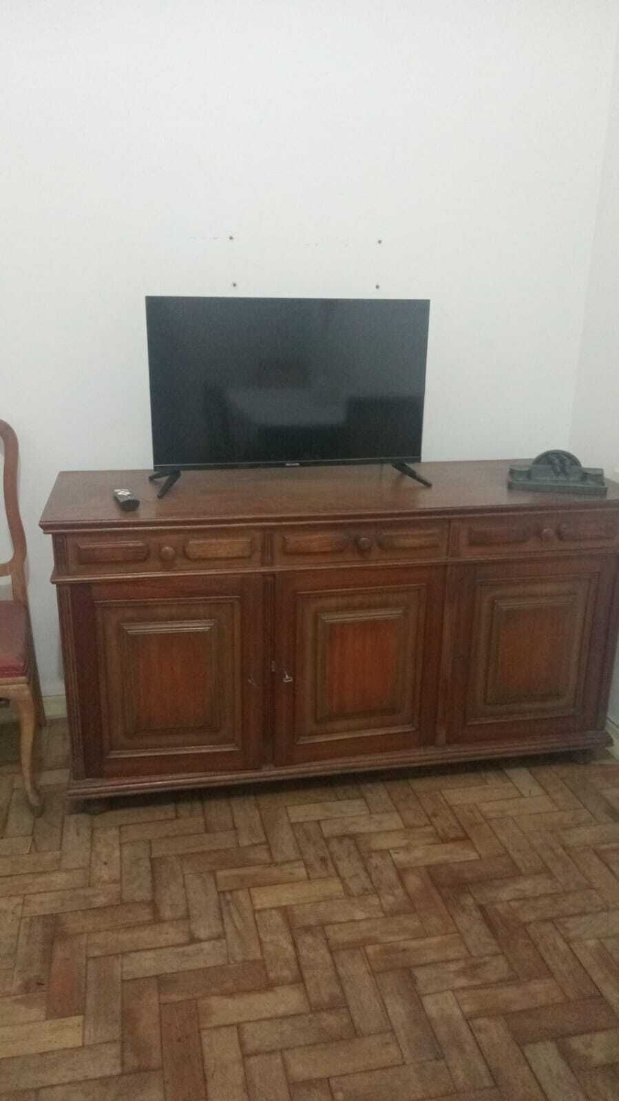 Ein Holzschrank mit einem Flachbildfernseher obenauf, einer Fernbedienung und einem Telefon auf der rechten Seite.