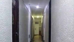Un pasillo largo y estrecho con paredes blancas y suelo de baldosas, que conduce a una puerta al final.