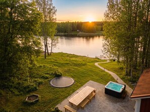 A lakeside patio with a hot tub, a wooden bench, and a circular fire pit.