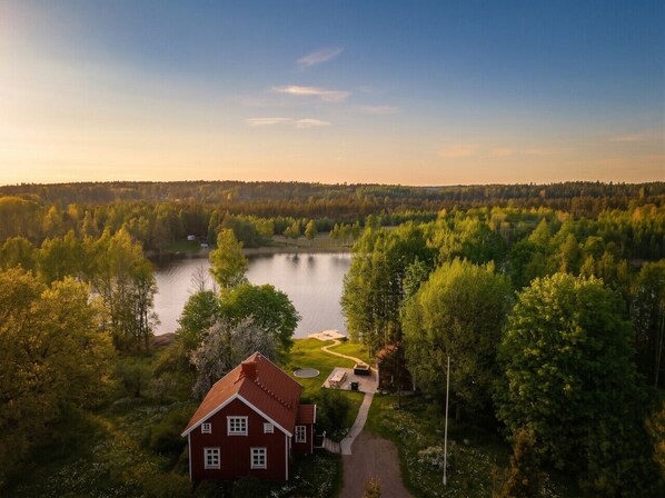 Une maison avec un toit rouge, entourée d’une forêt et d’un lac.