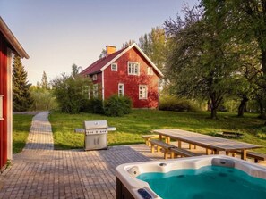 Un jardin avec un jacuzzi, un barbecue, une table de pique-nique et une maison rouge.
