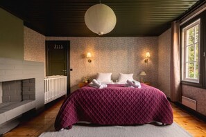 Une chambre à coucher avec un lit, une cheminée, deux lampes fixées au mur et une grande fenêtre.