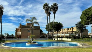 Una piscina rodeada de césped y palmeras, con un edificio al fondo.