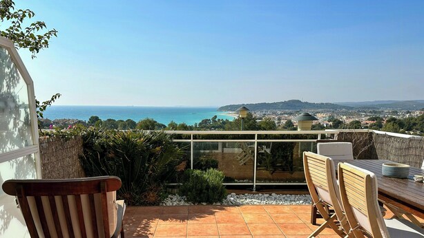 Una terraza con vistas al mar, un área de comedor con sillas y una mesa, y una partición de cristal.