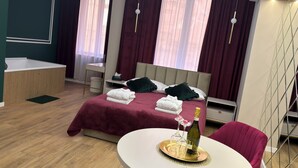 Ein Hotelzimmer mit einem Bett, einem Nachttisch, einem kleinen Schreibtisch, einem runden Tisch mit Flasche und Gläsern sowie einem Sessel.