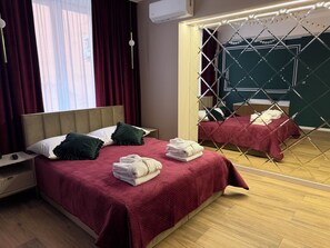 Habitació d'hotel amb un llit, una tauleta de nit, un mirall i una finestra amb cortines.