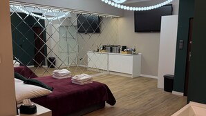 Ein modernes Hotelzimmer mit Holzboden, einem großen Bett mit roter Bettdecke, einem weißen Nachttisch, einem weißen Badezimmer mit Badewanne und einem an der Wand befestigten Fernseher.