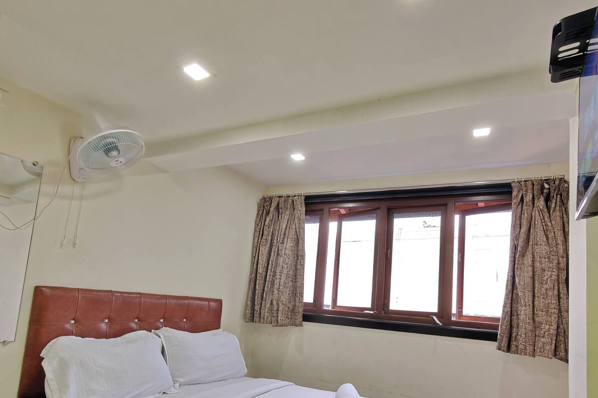 A neatly made bed with white linens, a wooden headboard, a ceiling fan, and a window with curtains.