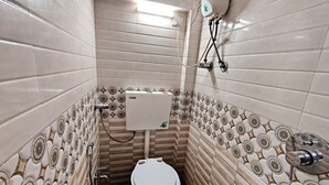 Een kleine, smalle badkamer met toilet, een aan de muur bevestigde boiler en betegelde wanden.