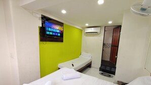 Een hotelkamer met een bed, een aan de muur bevestigde televisie, een airconditioning en een deur naar een badkamer.