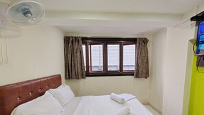 Een netjes opgemaakt bed met witte lakens, een bruin hoofdbord en een raam met gordijnen.