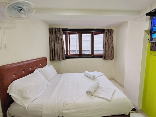 A neatly made bed with white linens, a brown headboard, and a window with curtains.