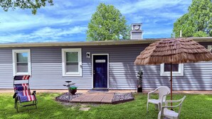 A house with a blue door, a thatched umbrella, a lawn chair, and a flag-adorned lounge chair. - Captain’s Quarters- charming studio apartment in the countryside (Berlin Center)