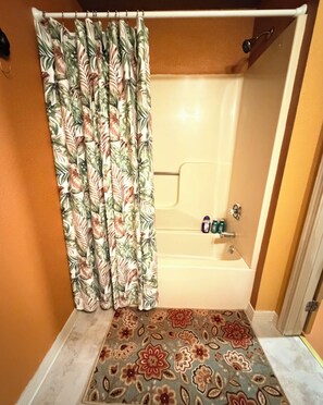 Ein Badezimmer mit Dusche, einem Duschvorhang mit Blumenmuster und einer Fußmatte mit Muster.