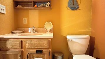 A bathroom with a wooden vanity, a sink, a mirror, a toilet, and a trash can.