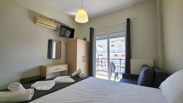 A hotel room with a bed, a TV, a wardrobe, a mirror, and a balcony with a table and chairs. - HOTEL GALINI  (Katerini)