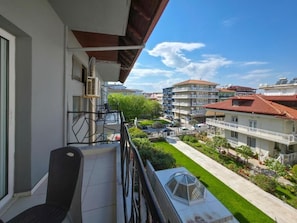 A balcony with a chair, a window, and a view of a residential area with buildings and a green lawn. - HOTEL GALINI (Katerini)