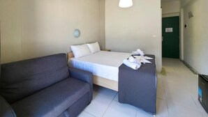 A room with a bed, a sofa, a small table, a hanging light fixture, and a door in the background. - HOTEL GALINI  (Katerini)