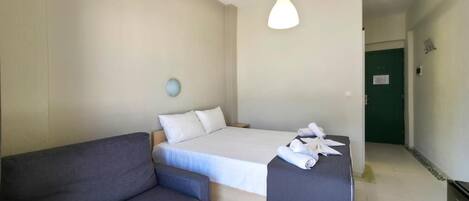 Een kamer met een bed, een bank, een tafeltje, een hanglamp en een deur op de achtergrond.