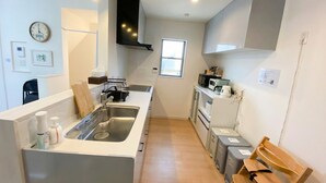 Una cocina compacta con un lavamanos, microondas y armarios, una banca de madera y un reloj en la pared.