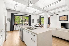 A modern kitchen with a central island, a dining area with a sofa, and large windows with curtains. - Renovated Warehouse Conversion In Heart Of Sydney! (Dawes Point)