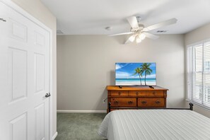 Ein Schlafzimmer mit einem Bett, einem hölzernen Schminktisch, einem Deckenventilator, einem Strandbild und einer Tür.
