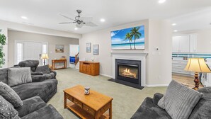 A living room with a fireplace, a ceiling fan, and a painting of a beach scene. - Saltwater Heaven (Rehoboth Beach)