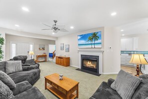 Ein Wohnzimmer mit Kamin, Deckenventilator und einem Strandbild.