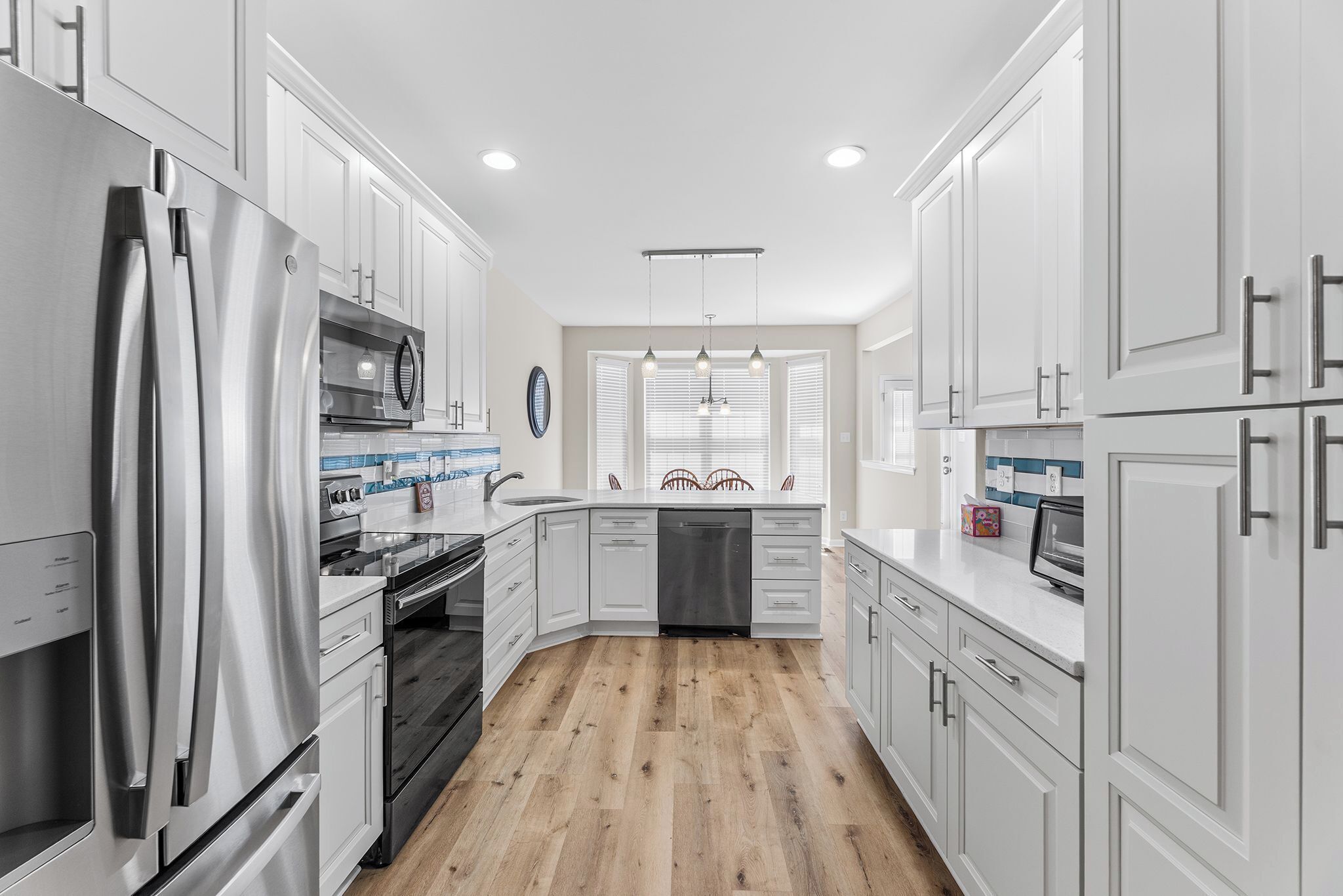 A modern kitchen with white cabinets, stainless steel appliances, and a wooden floor.