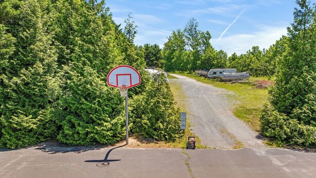 A basketball hoop, a gravel path, and a trailer in a wooded area. - Saltwater Heaven (Rehoboth Beach)