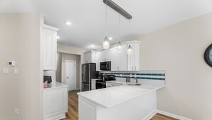 A modern kitchen with white cabinetry, a large island, pendant lighting, and a microwave. - Saltwater Heaven (Rehoboth Beach)