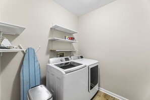 A laundry room with a washer and dryer, shelves with items, and a hanging blue garment. - Saltwater Heaven (Rehoboth Beach)