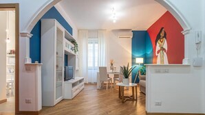 A living room with a TV, a dining table, and chairs. There is a painting on the wall and a plant on the table. - Casa Abeba (Rome)
