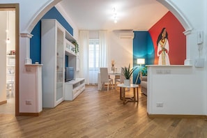 A living room with a TV, a dining table, and chairs. There is a painting on the wall and a plant on the table. - Casa Abeba (Rome)
