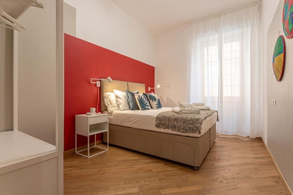 A bedroom with a bed, bedside table, and a red accent wall.
