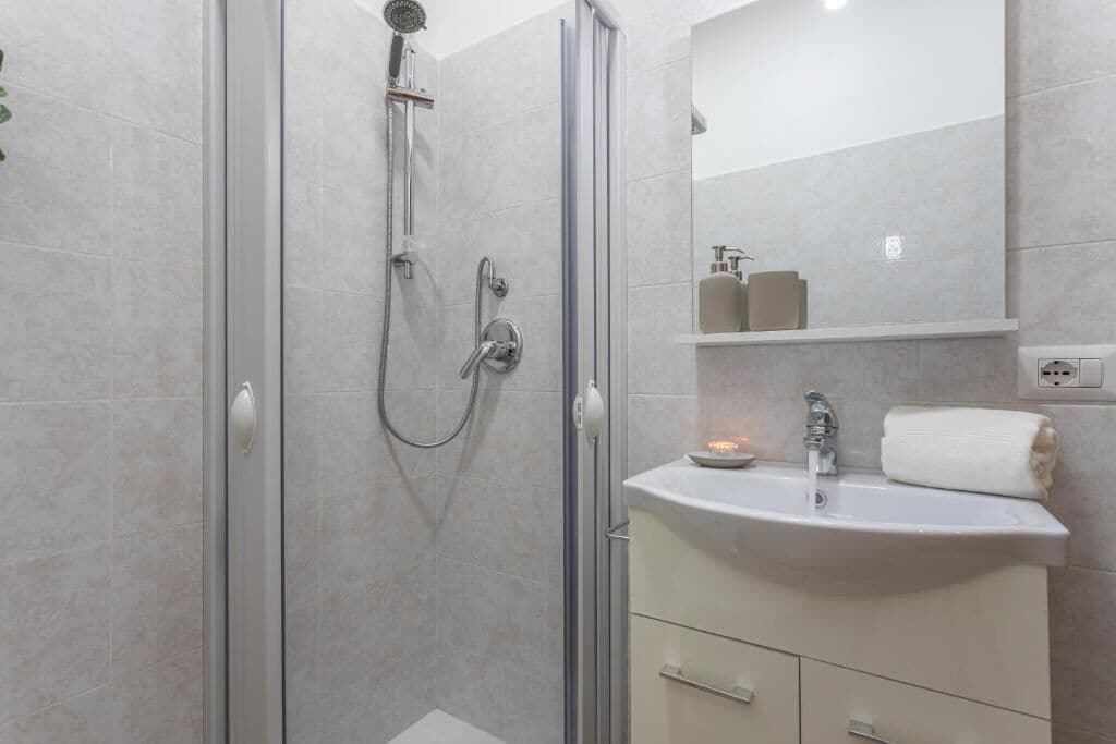 A modern bathroom with a glass-enclosed shower, a white sink, and a mirror above it.