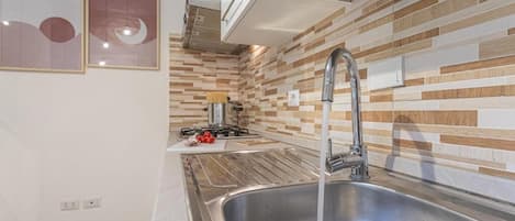 Una cocina moderna con un lavamanos de acero inoxidable, una estufa a gas y un salpicadero de azulejos.