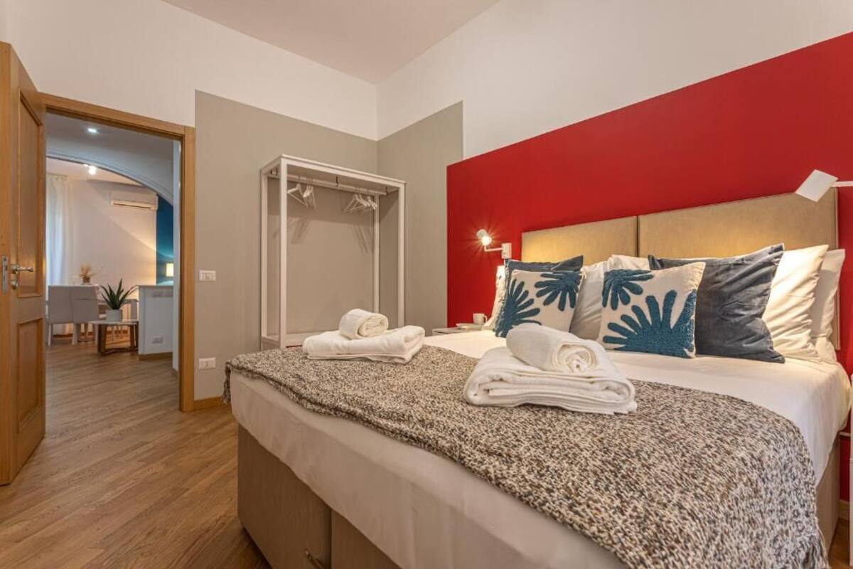 Una habitación de hotel con una cama, una pared de acento roja, un espejo y una puerta que da a un baño.