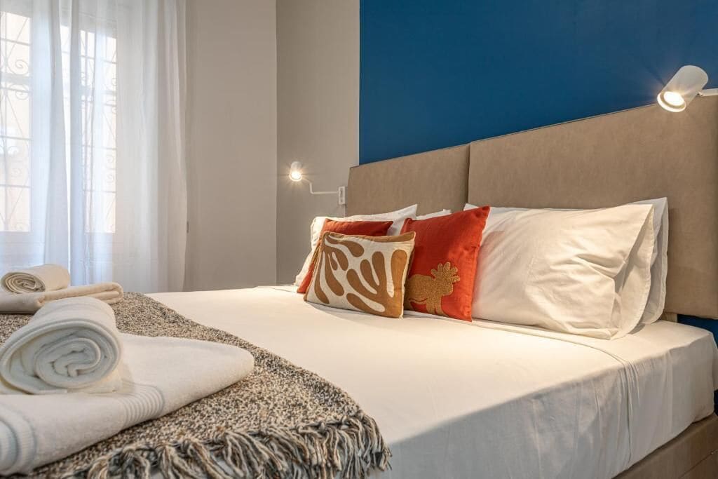Ein ordentlich bezogenes Bett mit Kopfteil, ein gerolltes Handtuch und eine Decke auf dem Boden.