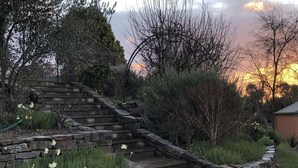 Uma escadaria de pedra leva a uma casa, cercada por vegetação e árvores.
