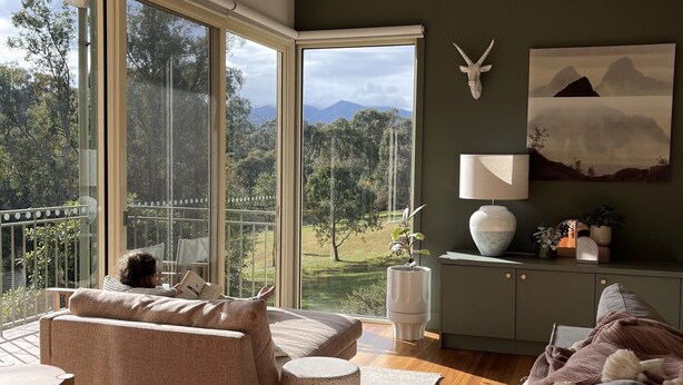 Um quarto com uma grande janela, um sofá, uma luminária e um armário com objetos decorativos.