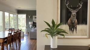 Uma área de refeições com mesa e cadeiras de madeira, uma janela grande com vista e um quadro de um veado na parede.