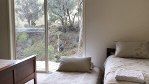 Quarto com cama, mesa de cabeceira e janela com vista para árvores e um morro.