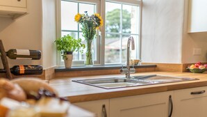 A kitchen with a double sink, a window with a view, a wine bottle, and a bowl of fruit. - Ficerdy -  a self catering cottage that sleeps 6 guests  in 3 bedrooms (Llandwrog)