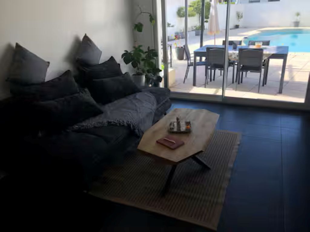 Een woonkamer met een bank, een salontafel en uitzicht op een buitenzwembad.
